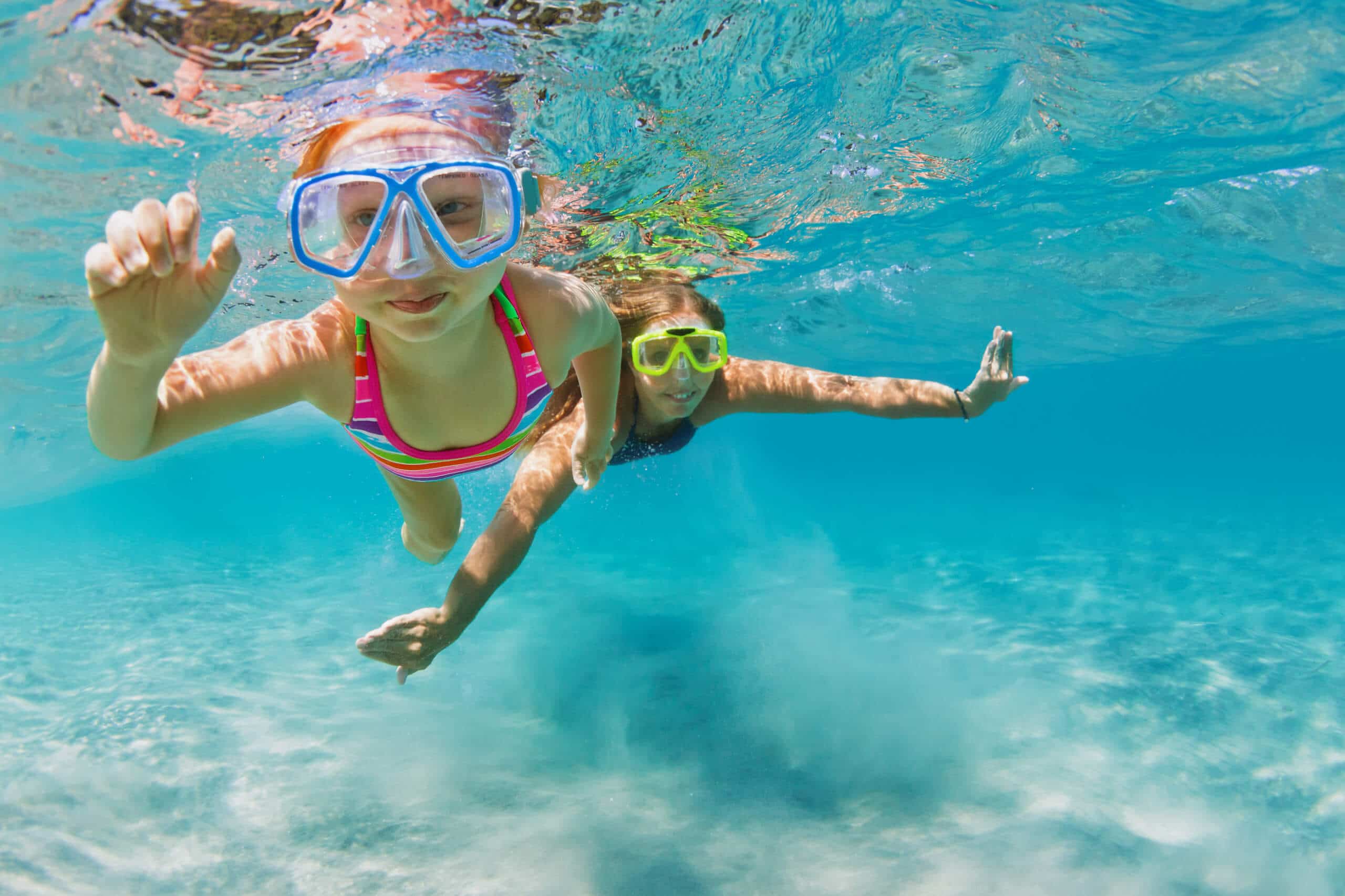 Young mother with child in snorkeling mask dive in coral reef sea lagoon to explore underwater world. Family travel lifestyle in summer adventure camp. Swimming activities on beach vacation with kids.