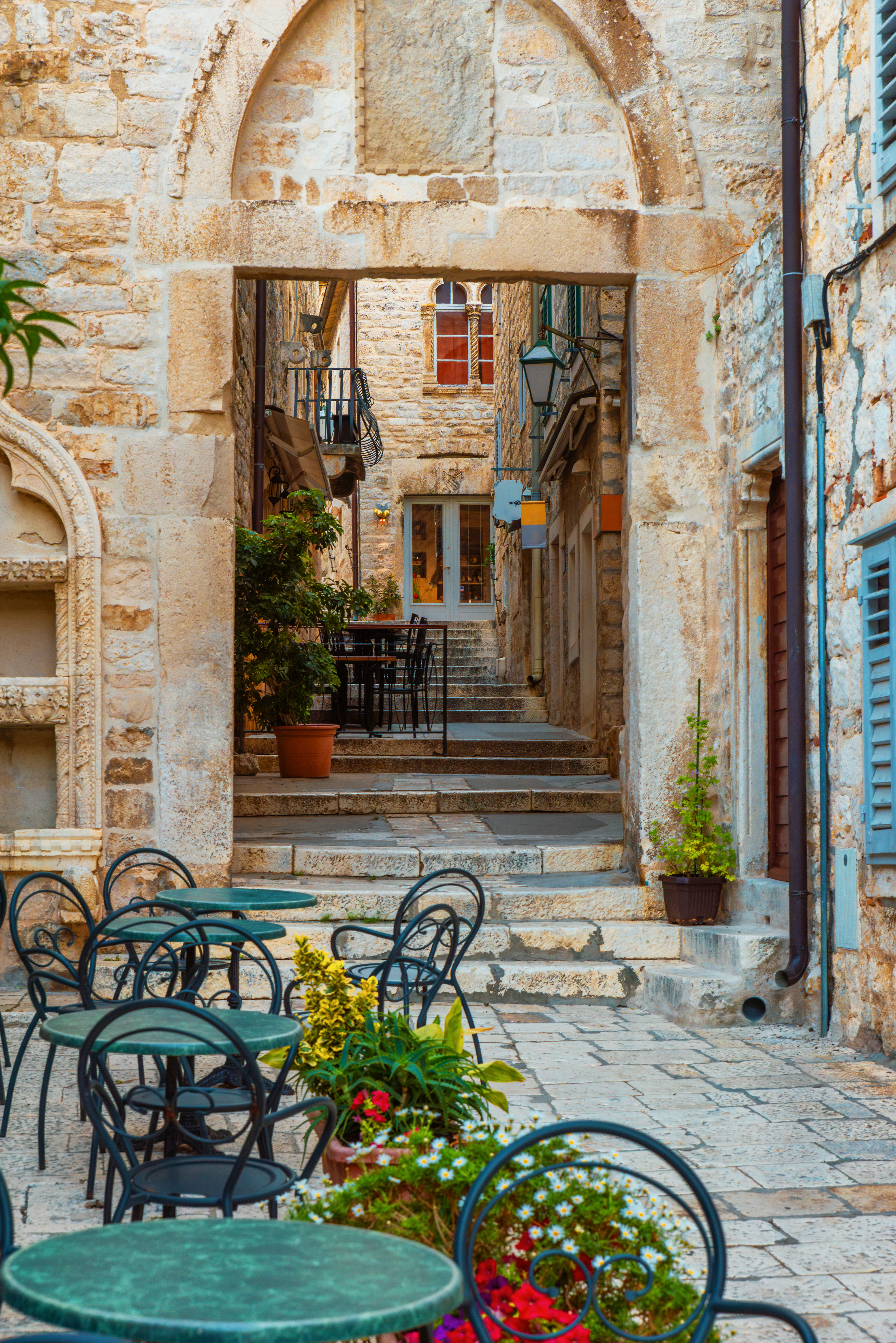 Sidewalk cafe with tables and chairs outside in old cozy street in the in old medieval town Hvar in outdoor restaurant with nobody, Dalmatia, Croatia. Vertical orientation. Popular travel and tourist destination on summer vacations.
